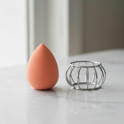 Peach Coral teardrop makeup sponge beside silver wire cage holder on white marble